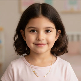 Girl modelling gold kids double name necklace on anchor chain - Dahlia font