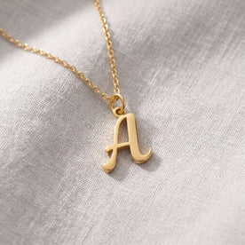 Personalised gold initial necklace with the letter A in the Bella style, laid flat on linen, showing the whole necklace.