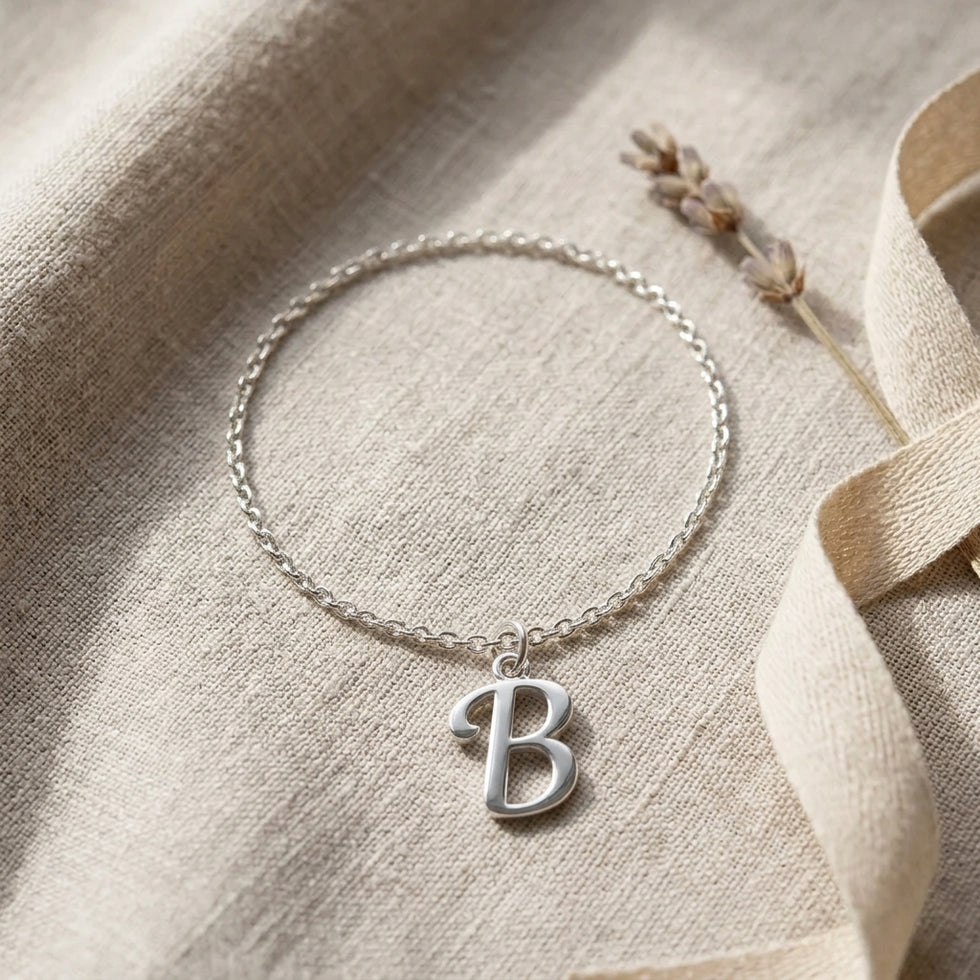 Personalised silver initial bracelet with the letter B in the Bella style, styled on linen with dried flowers.