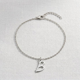 Personalised silver initial bracelet with the letter B in the Eva style, laid flat on linen, showing the whole bracelet.