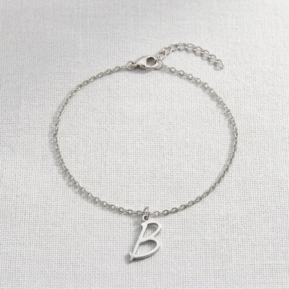 Personalised silver initial bracelet with the letter B in the Eva style, laid flat on linen, showing the whole bracelet.