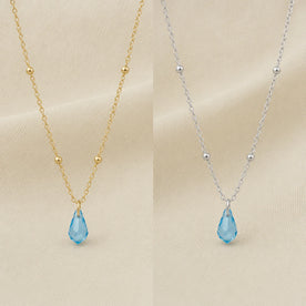 Side-by-side comparison of the birthstone crystal drop necklace in 18ct gold and silver, both with an aquamarine teardrop pendant