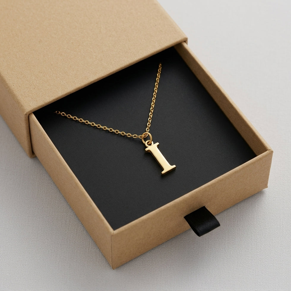 Personalised gold initial necklace with the letter I in the Mia style, presented in the kraft gift box it is sent in.