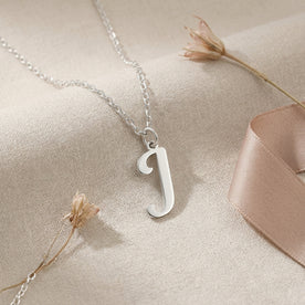 Personalised silver initial necklace with the letter J in the Bella style, styled on linen with dried flowers.