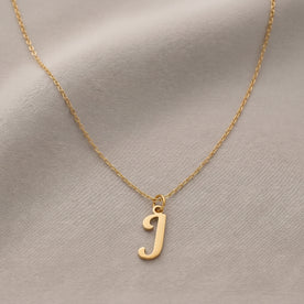 Personalised gold initial necklace with the letter J in the Bella style, laid flat on linen, showing the whole necklace.