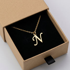 Personalised gold initial necklace with the letter N in the Mia style, presented in the kraft gift box it is sent in.