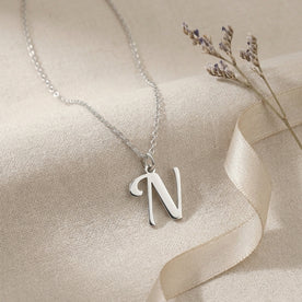 Personalised silver initial necklace with the letter N in the Bella style, styled on linen with dried flowers.