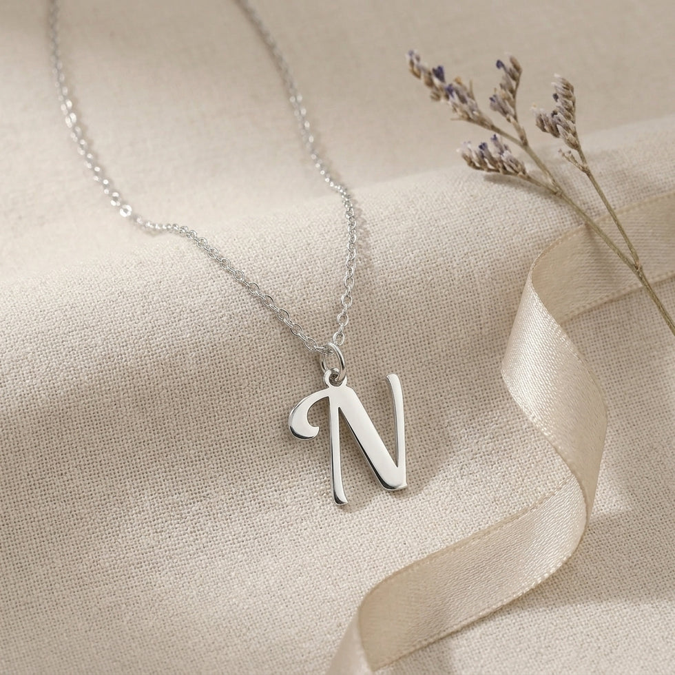 Personalised silver initial necklace with the letter N in the Bella style, styled on linen with dried flowers.
