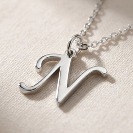 Personalised silver initial necklace with the letter N in the Zara style, close up, showing the polished cut edge and the thickness of the metal.