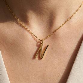 Personalised gold initial necklace with the letter N in the Eva style, worn at the base of the throat.