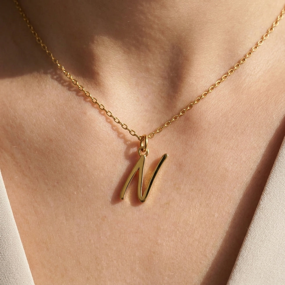 Personalised gold initial necklace with the letter N in the Eva style, worn at the base of the throat.