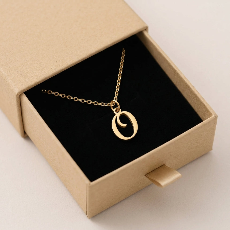 Personalised gold initial necklace with the letter O in the Mia style, presented in the kraft gift box it is sent in.