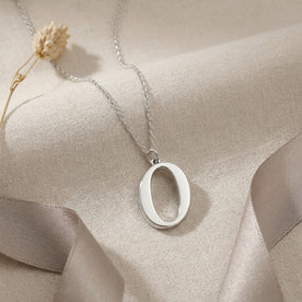 Personalised silver initial necklace with the letter O in the Bella style, styled on linen with dried flowers.