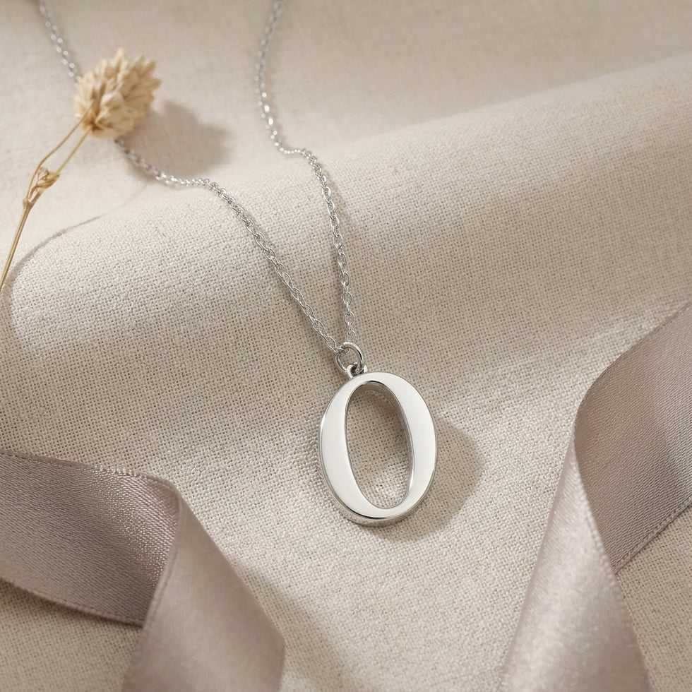 Personalised silver initial necklace with the letter O in the Bella style, styled on linen with dried flowers.