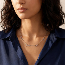 Woman in a navy satin shirt wearing a silver personalised quadruple name necklace with script names - Zara font