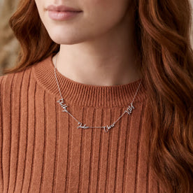 Woman in a rust ribbed sweater wearing a silver personalised quadruple name necklace with script names - Zara font