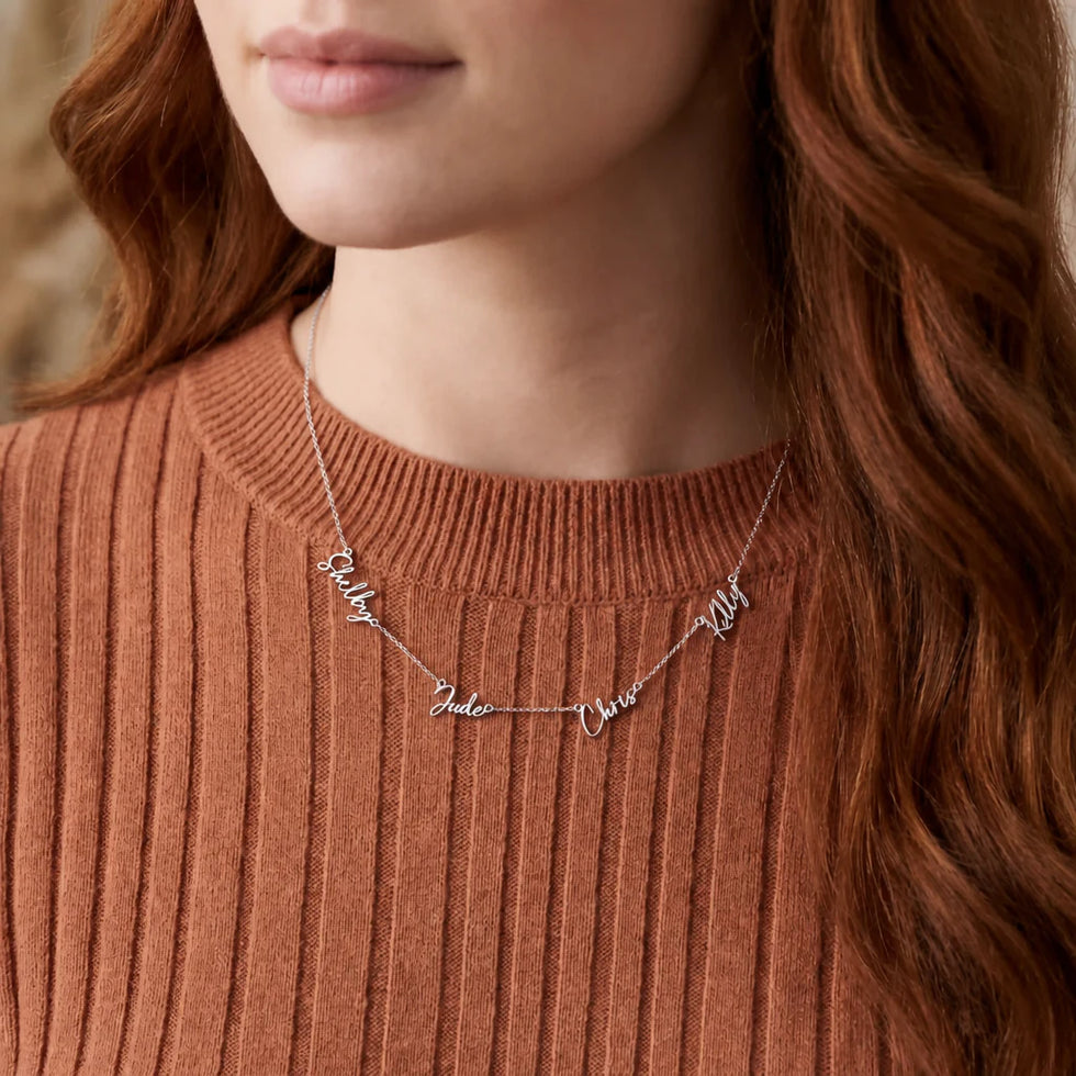 Woman in a rust ribbed sweater wearing a silver personalised quadruple name necklace with script names - Zara font