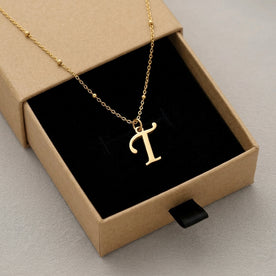 Personalised gold initial necklace with the letter T in the Mia style, presented in the kraft gift box it is sent in.