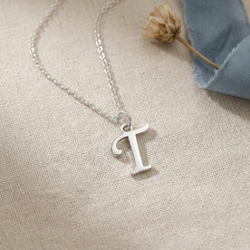 Personalised silver initial necklace with the letter T in the Bella style, styled on linen with dried flowers.