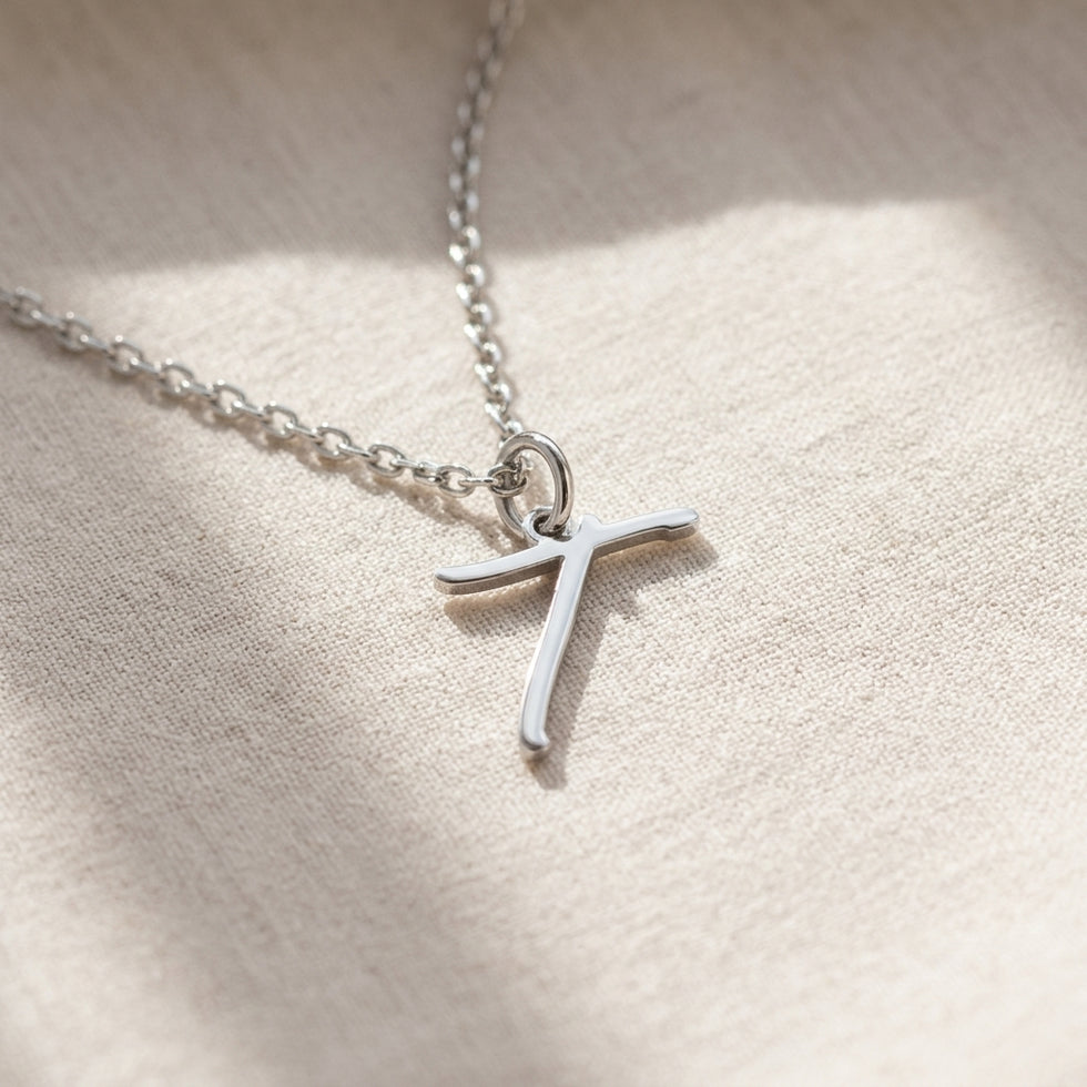 Personalised silver initial necklace with the letter T in the Eva style, laid flat on linen, showing the whole necklace.