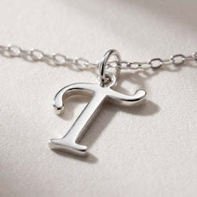 Personalised silver initial necklace with the letter T in the Zara style, close up, showing the polished cut edge and the thickness of the metal.