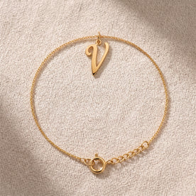 Personalised gold initial bracelet with the letter V in the Bella style, laid flat on linen, showing the whole bracelet.