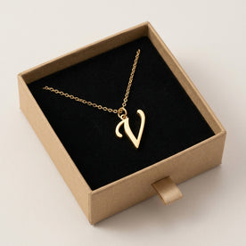 Personalised gold initial necklace with the letter V in the Mia style, presented in the kraft gift box it is sent in.