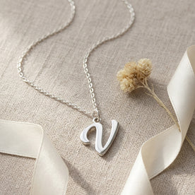 Personalised silver initial necklace with the letter V in the Bella style, styled on linen with dried flowers.
