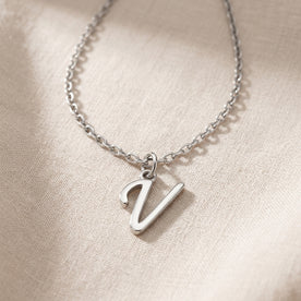 Personalised silver initial necklace with the letter V in the Eva style, laid flat on linen, showing the whole necklace.