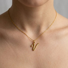 Personalised gold initial necklace with the letter V in the Eva style, worn at the base of the throat.